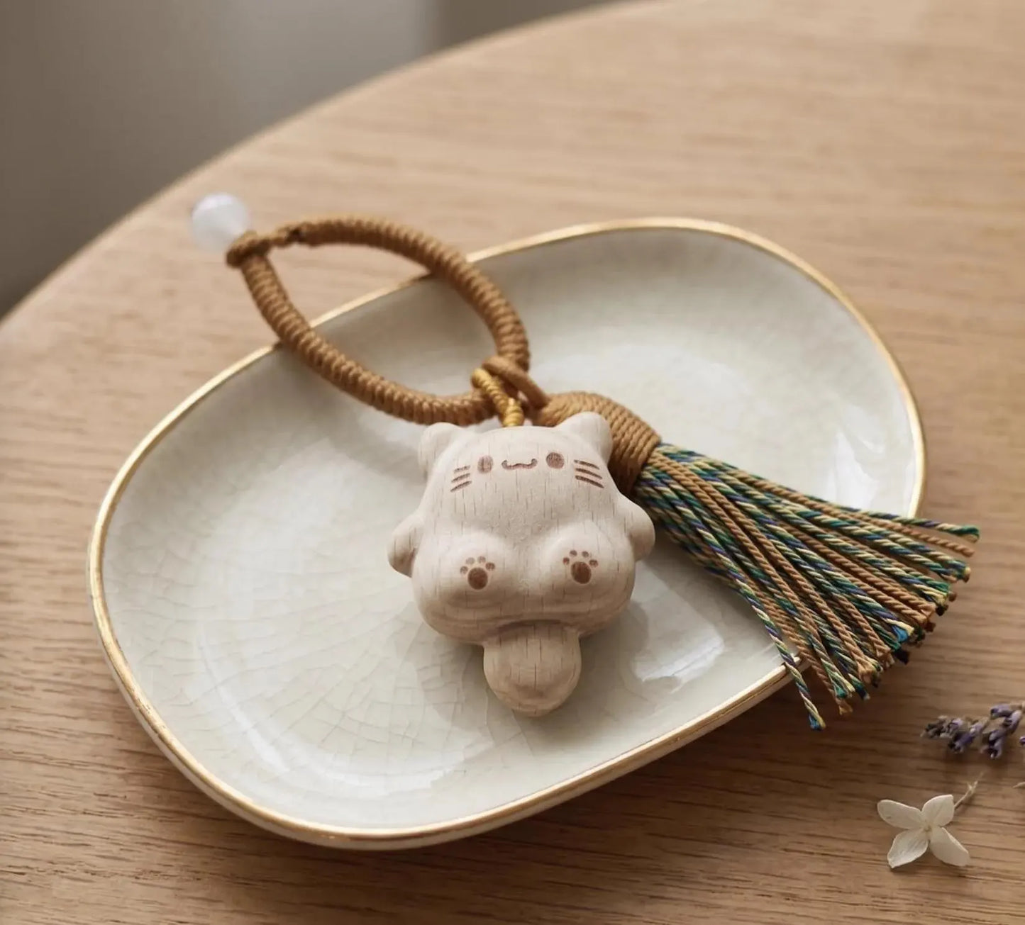 A hand holding a small carved wooden cat charm keychain with a brown braided cord and tassel against a plain light background. Handmade Wooden Cat Charm - Cute Kawaii Cat Bag Pendant, Minimalist Wood Keychain, Car Decor, Phone Strap, Unique Gift for Cat Lovers, Gifts