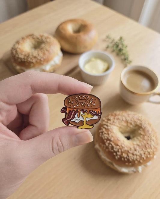 Elevate your accessory game with the ultimate breakfast staple! This Bacon, Egg, and Cheese Bagel Enamel Pin is a must-have for every brunch enthusiast, bagel lover, and foodie collector. Featuring a perfectly rendered "everything" bagel overflowing with crispy bacon, a golden over-easy egg, and melted cheese, this pin looks good enough to eat.Bacon Egg and Cheese Bagel Enamel Pin - Cute Breakfast Foodie Lapel Pin, Everything Bagel Jewelry, Gourmet Food Gift for Chef & Brunch Lover