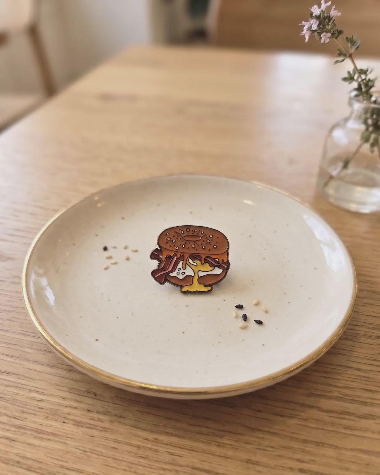 Elevate your accessory game with the ultimate breakfast staple! This Bacon, Egg, and Cheese Bagel Enamel Pin is a must-have for every brunch enthusiast, bagel lover, and foodie collector. Featuring a perfectly rendered "everything" bagel overflowing with crispy bacon, a golden over-easy egg, and melted cheese, this pin looks good enough to eat.Bacon Egg and Cheese Bagel Enamel Pin - Cute Breakfast Foodie Lapel Pin, Everything Bagel Jewelry, Gourmet Food Gift for Chef & Brunch Lover