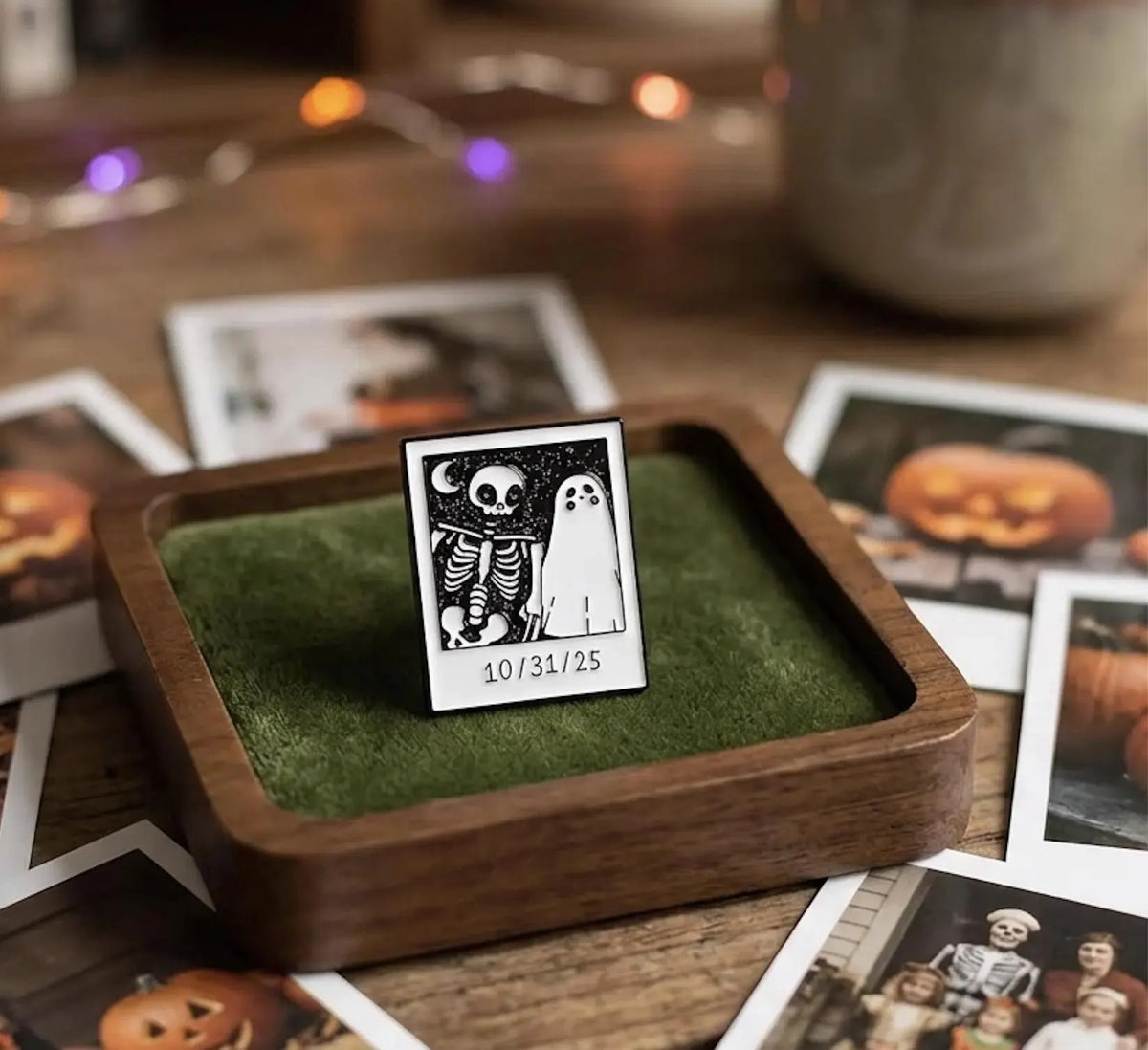 A canvas tote bag laid on a wooden surface with dried leaves and a knit blanket nearby. On the bag are several small enamel pins: a square black-and-white skeleton-and-ghost design with the date '10. Spooky Ghost and Skeleton Enamel Pin - Cute Halloween Polaroid Lapel Pin - Aesthetic Gothic Jewelry - Retro Spooky Season Gift for friends