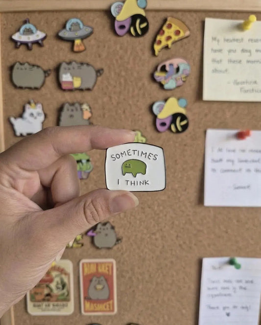 A hand holds a small enamel pin with a green cartoon creature and the text 'SOMETIMES I THINK' in front of a yellow tote bag and a blurred desk background with books. Cute Frog Enamel Pin, “Sometimes I Think” Meme Pin, Funny Relatable Gift, Mental Health Pin, Kawaii Green Pin, ADHD Pin, Gift for Friends