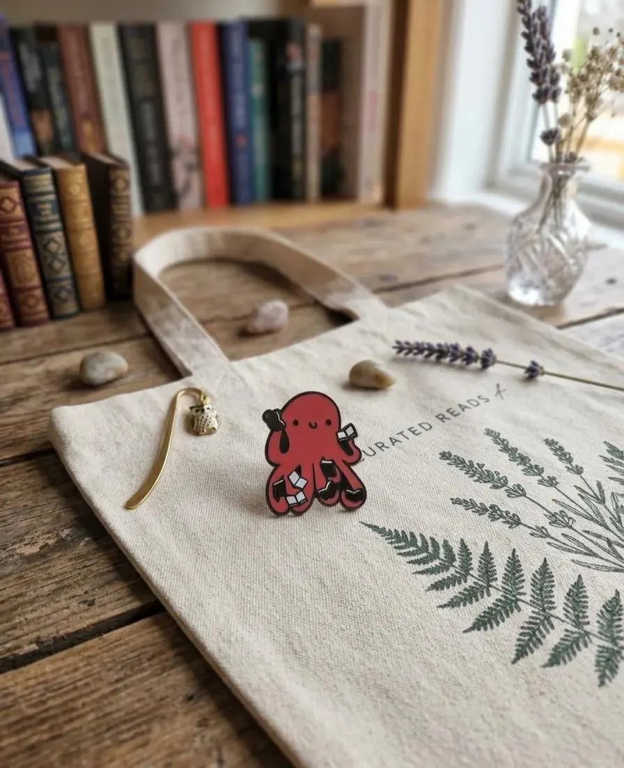 A red octopus-shaped enamel pin with black outlines and white accents, displayed on a wooden bookshelf next to books and a small glass vase with dried flowers. Red Octopus Reading Book Enamel Pin, Cute Bookworm Brooch, Nerdy Library Jewelry, Academic Animal Badge, Reader Gift, Teacher Appreciation