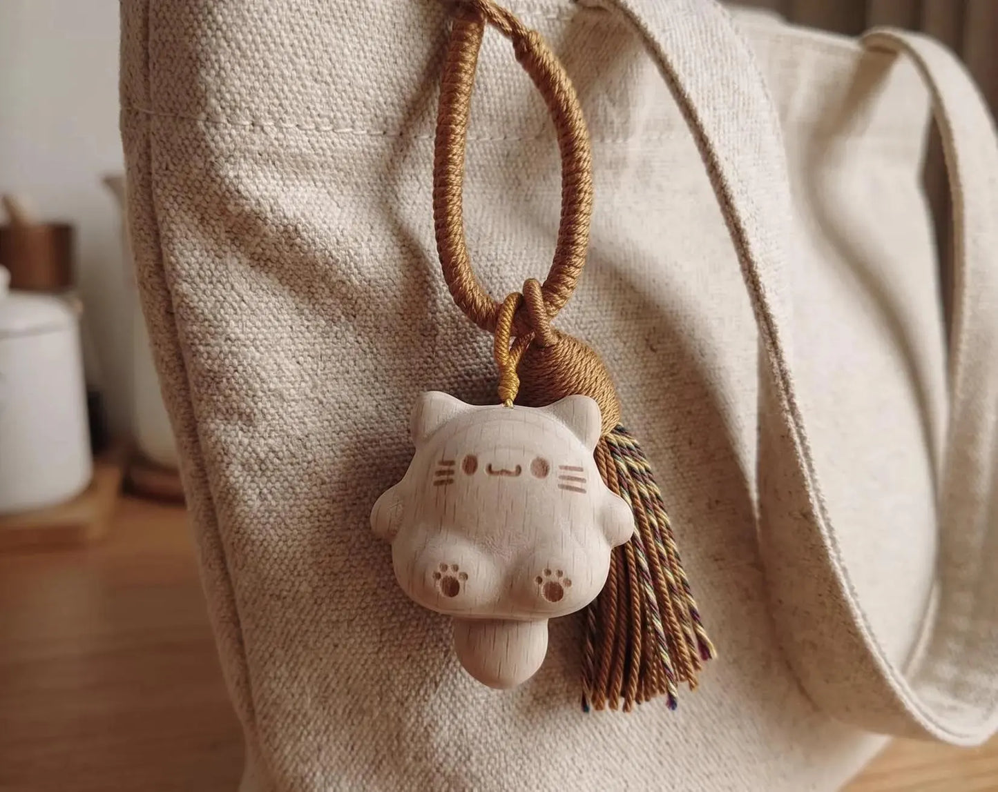 A hand holding a small carved wooden cat charm keychain with a brown braided cord and tassel against a plain light background. Handmade Wooden Cat Charm - Cute Kawaii Cat Bag Pendant, Minimalist Wood Keychain, Car Decor, Phone Strap, Unique Gift for Cat Lovers, Gifts
