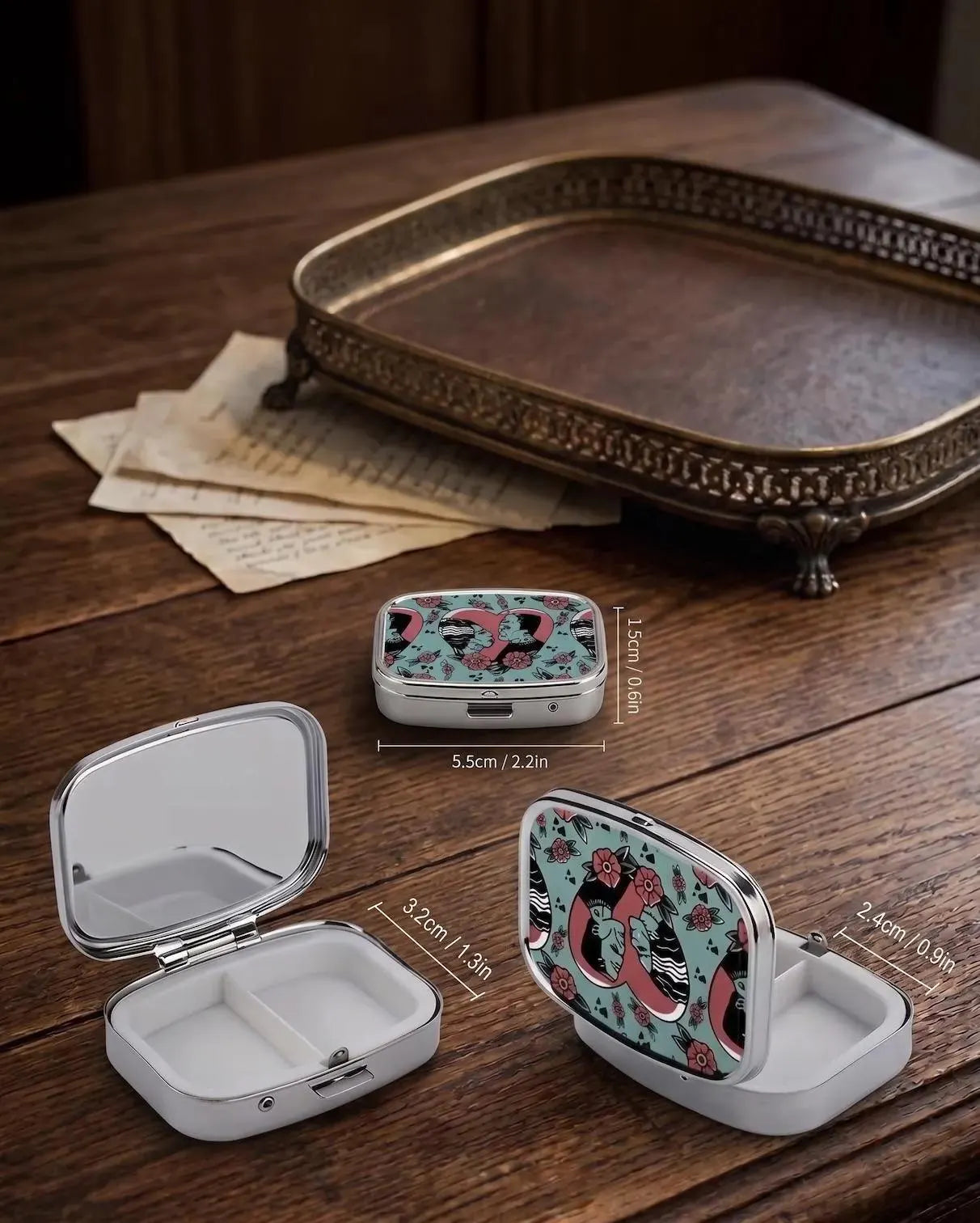 A hand holding a small rectangular metal case with a colorful pattern featuring a pink heart, black and white zebra stripes, and red flowers on a light blue background, set against a blurred background of vintage books and a wooden table. Bride of Frankenstein Pill Box Organizer, Goth Travel Pill Case for Purse, Spooky Horror Gift for Her, Aesthetic Gothic Jewelry Pill Box