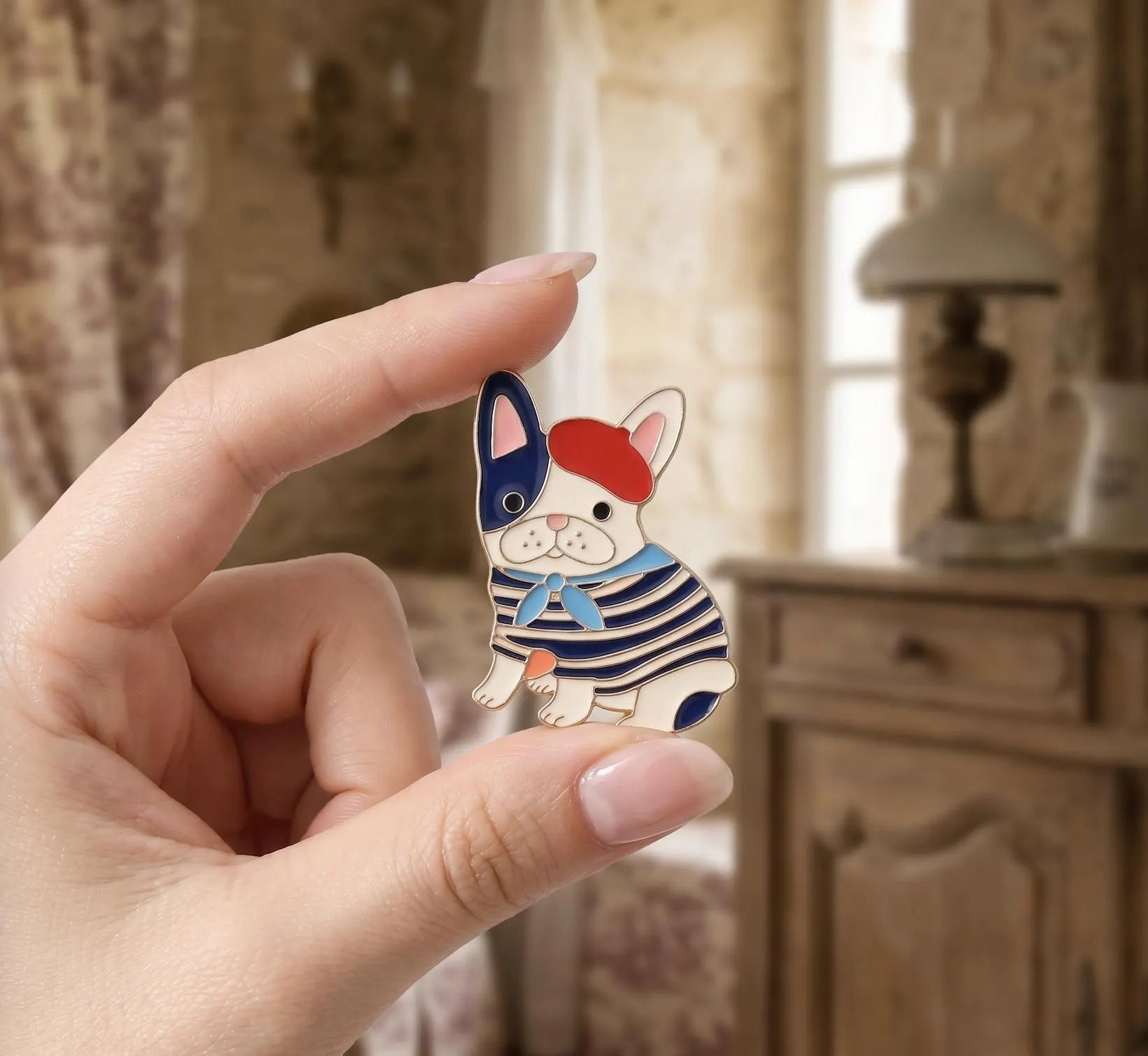 A small enamel lapel pin shaped like a French bulldog wearing a red beret and navy-and-white striped sweater, displayed on a hammered gold dish on a rustic wooden table with a thimble and dried rose nearby. French Bulldog Enamel Pin, Cute Frenchie in Beret Lapel Pin, Dog lovers, Aesthetic Animal Brooch, Parisian Style, Gift for Dog Mom, Cute Pin French Bulldog Enamel Pin, Cute Frenchie in Beret Lapel Pin, Parisian Dog Lover Gift, Dog Mom Backpack Flair, Aesthetic Animal Brooch Gift