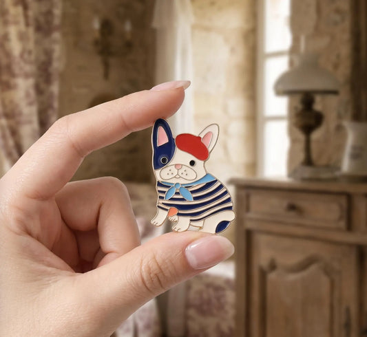 A small enamel lapel pin shaped like a French bulldog wearing a red beret and navy-and-white striped sweater, displayed on a hammered gold dish on a rustic wooden table with a thimble and dried rose nearby. French Bulldog Enamel Pin, Cute Frenchie in Beret Lapel Pin, Dog lovers, Aesthetic Animal Brooch, Parisian Style, Gift for Dog Mom, Cute Pin French Bulldog Enamel Pin, Cute Frenchie in Beret Lapel Pin, Parisian Dog Lover Gift, Dog Mom Backpack Flair, Aesthetic Animal Brooch Gift