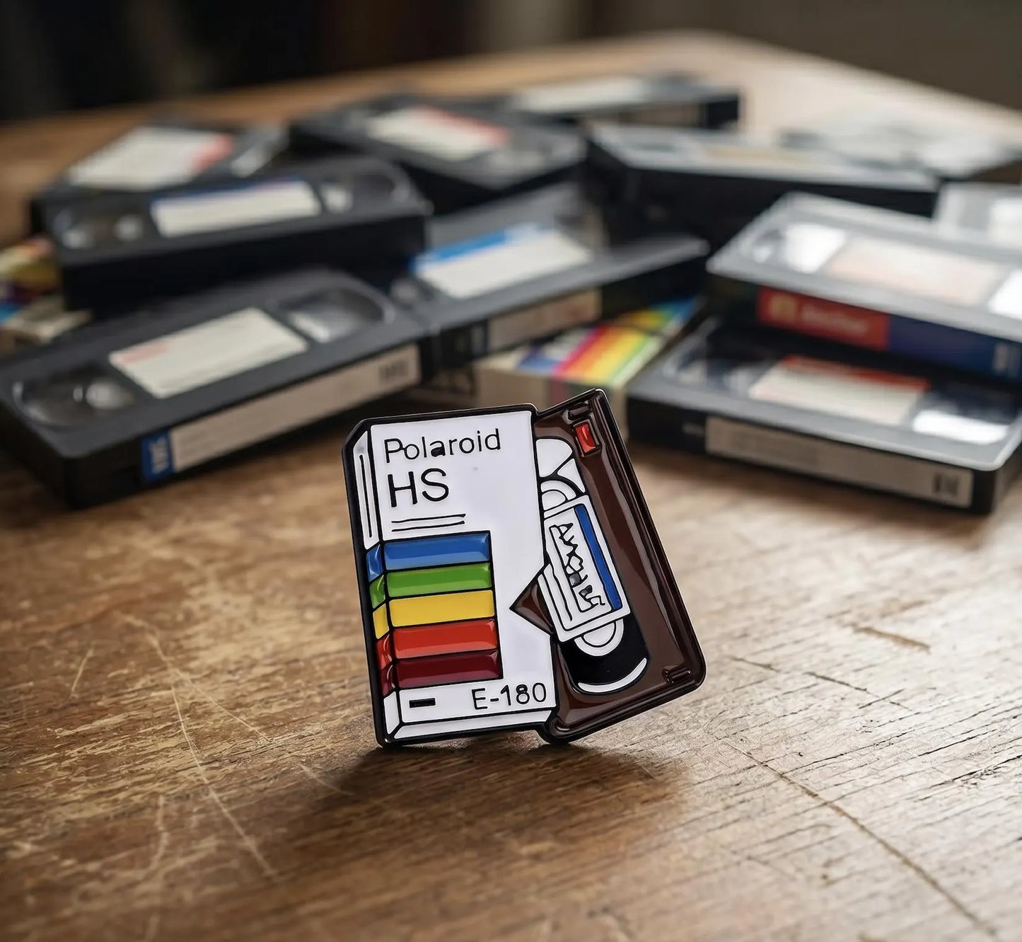 A hand holding a miniature Polaroid H5 camera memory card, with a blurred vintage camera and film strip in the background. Retro VHS Tape Enamel Pin | Vintage VCR Video Cassette Badge | 80s 90s Nostalgia Movie Lover Gift | Aesthetic Rainbow Movie Pins, Film Lover
