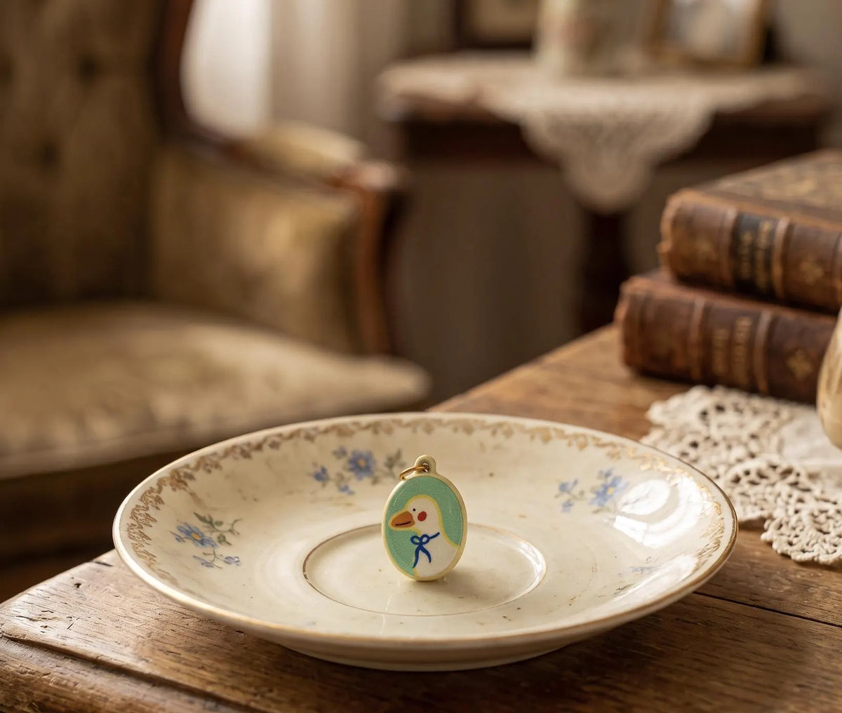 A hand holding a small oval charm with a yellow cord and tassel, featuring a cartoon bird design, against a softly blurred indoor background. Collectable Vintage Duck Charm in Bowtie, Delicate Oval Pendant, Retro Cottagecore Keychain Accessory, DIY Fashion, Duck Lovers Small Gift